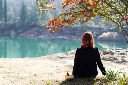 femme en noir de dos face à un lac avec un bol chantant 