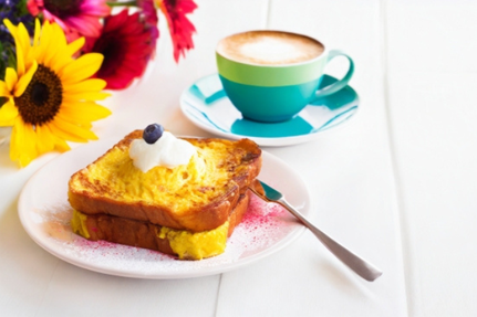 フレンチトーストのお皿とカフェラテのカップ。ひまわりとガーベラの花が飾られている。