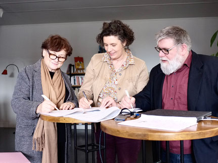 De gauche à droite, Béatrice Maisonnave (ARS), Sophie Lecointe (DRAC) et Philippe Demoulin (Les Singuliers Associés) signent les documents posés devant eux sur une table haute.