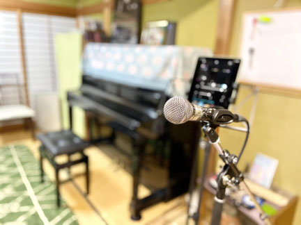荒井みな子ボイストレーニングstudy　飯田教室のレッスン室内写真,手前にマイクスタンド,その後にタブレットとスタンドピアノ<椅子が置かれている