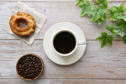 テーブルにコーヒー豆が盛り付けられた器、コーヒーの入ったカップ&ソーサ、ドーナツが並んでいる。アイビーの葉。