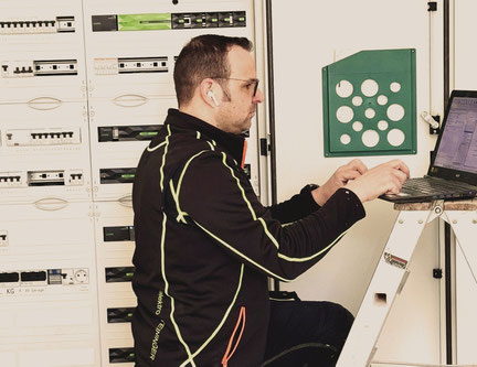Elektriker Thomas Steinberger kniet vor einem Laptop und prüft ein Netzwerk. 