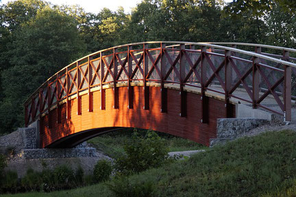 Geschwungene Holzbrücke die im Sonnenlicht über einen Graben führt
