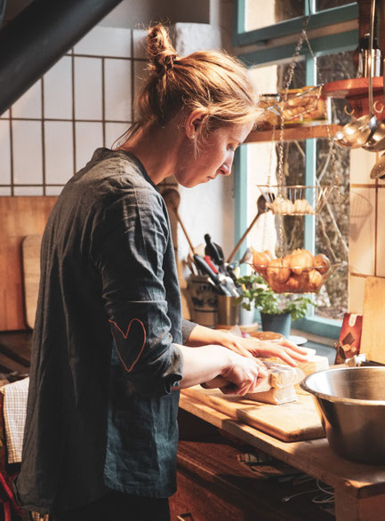 Frau (Maxine Morast) von der Seite beim achtsamen, vollwertig pflanzlichem Kochen bzw. Schneiden auf Holzbrett in der Küche des Seminarzentrums Grube Louise im Westerwald