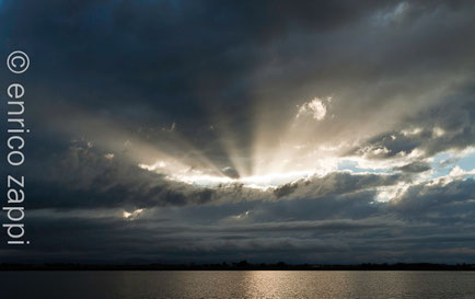Raggi di luce solare filtrano dalla grigia e fitta coltre di nubi sulle Saline di Cervia.