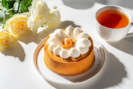 生クリームがたっぷりのったスポンジケーキ。紅茶のカップ。黄色と白色のバラの花。