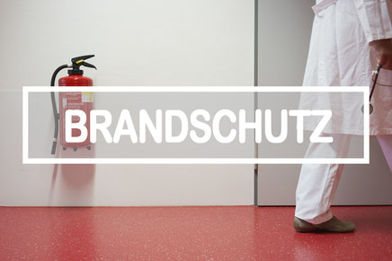 Arzt in Krankenhausflur mit Brandmelder an der Wand