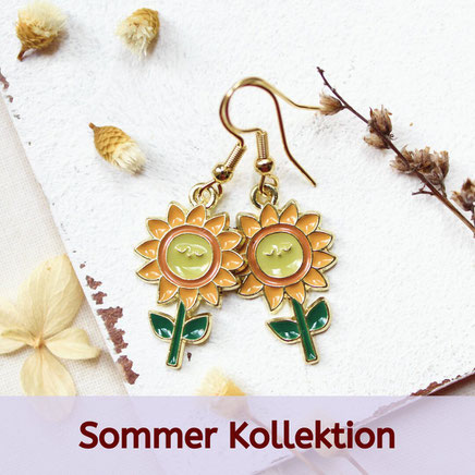 Zwei Sonnenblumen-Ohrringe auf weißem Hintergrund mit getrockneten Blumen. Text: "Sommer Kollektion".