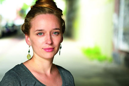 Das Bild zeigt die Autorin Alina Herbig mit grauem Longsleeve und Hochsteckfrisur.
