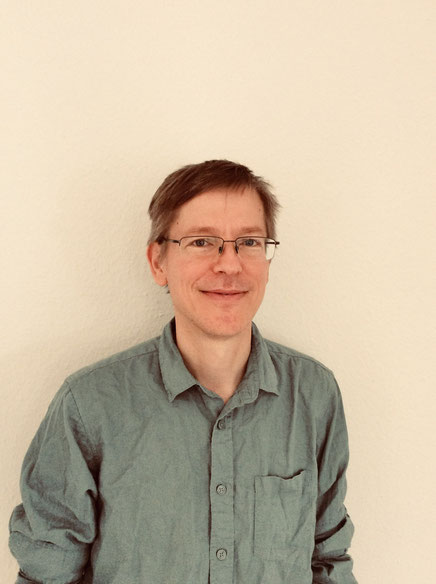 Der Übersetzer Marc Hermann trägt ein Leinenhemnd und eine Brille und lächelt in die Kamera.