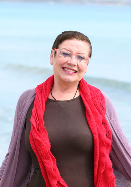 Das Bild zeigt die Autorin Kerana Angelova mit Brille und rotem Schal, die in die Kamera lächelt.