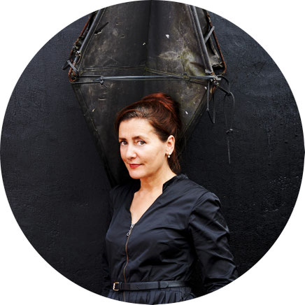 Das Bild zeigt die Autorin Anke Feuchtenberger mit roten, hochgesteckten Haaren und einem blauen Kleid.