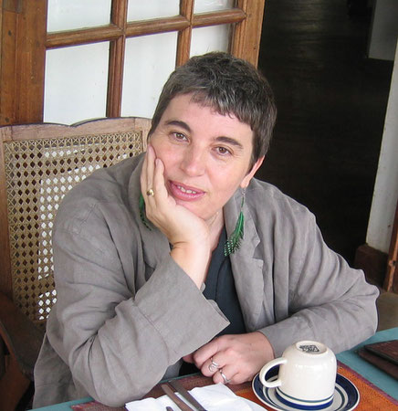 Das Bild zeigt die Übersetzerin Christiane Kayser am Kaffeetisch mit kurzen grauen Haaren und langen Federohrringen.