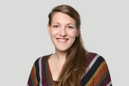 Das Bild zeigt Nora Locher. Die lächelt und hat einen langen Zopf und ein gestreiftes Oberteil.