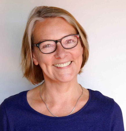 Das Bild zeigt die Übersetzerin Annette Kopetzki mit kurzen blonden Haaren und Brille, die in die Kamera lächelt.