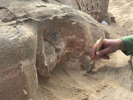 Archaeologist carefully removes layers of sand from sphinx head