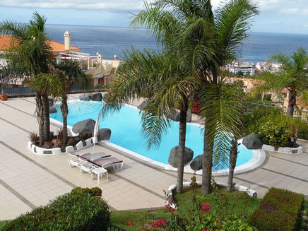 Auf dem Bild sieht man den abgerundeten Pool der Wohnanlage und im Hintergrund das Meer.
