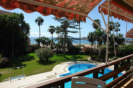 Blick vom Balkon in den Reich bepflanzte Gemeinschaftsgarten mit Pool und dem Strand im Hintergrund.