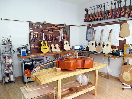 Bespoke luthier workshop featuring violins and guitars under construction with professional woodworking tools and instrument design plans.