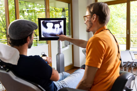 Arzt zeigt liegendem Patienten Röntgenbild von seinen Zähnen
