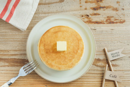 バターがのったパンケーキのお皿。フォーク。赤のラインがはいったキッチンクロス。