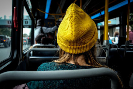 Frau mit gelber Mütze sitzt im Bus und spürt das bremsen