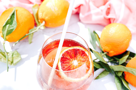 オレンジの輪切りが浮かんだオレンジジュースのグラス。葉っぱのついたオレンジの実。ピンク色のストール。