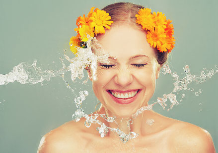 Lachende Frau mit Blumen im Haar und Wasser von der Seite