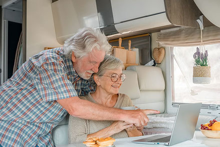 Älteres Ehepaar sitzt im Wohnmobil vor dem Laptop und ist glücklich 2026