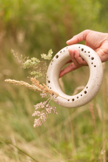 Beige ronde bloemenvaas met grassen erin, vastgehouden in de groene natuur