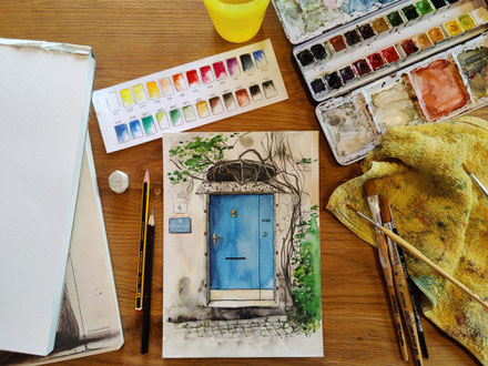 Aquarellbild von einer Haustür wird gemalt, um das Bild herum liegen Malutensilien auf dem Tisch
