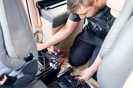 Ein Techniker von Camperwelt Fischer führt Wartungsarbeiten an einem Wohnmobil durch.
