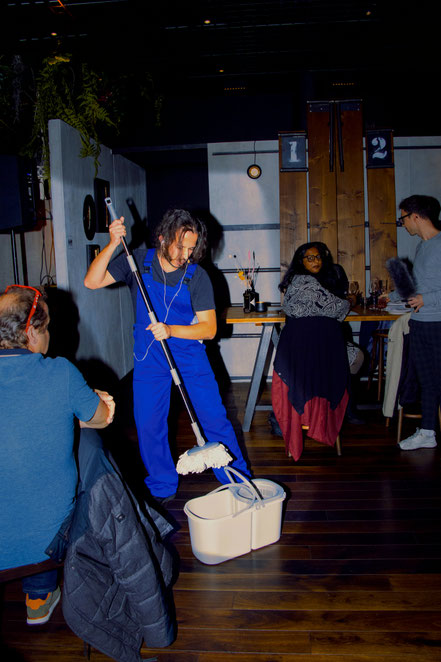 Ein Mann im blauen Overal putzt im Restaurant in mitten der Gäste den Boden. Beseitigt er Beweisspuren des Kriminalfalls "Tatort"? Das Krimmidinner mit Schauspielern in Eurem Wunschlokal in Bern sorgt garantiert für Spannung an eurem Anlass!