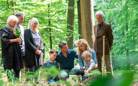 Trauernde Angehörige stehen und hocken um eine Friedwald-Gingkoblatt-Urne in einem Mischwald