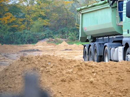 LKW schütten mit Sand eine Landschaft zu.
