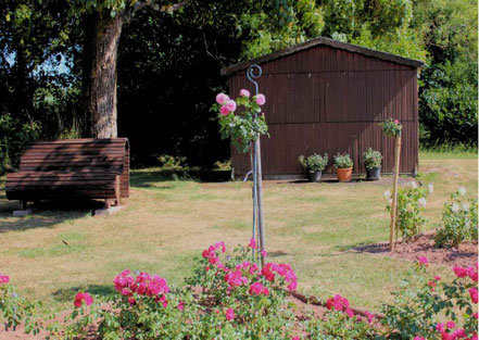 Gartenhütte und Bank vor dem Baum umgeben von Rosen in Welschbach im Saarland