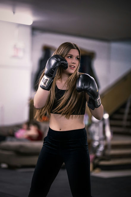 Lächelnde junge Frau mit Boxhandschuhen im Training am Boxsack