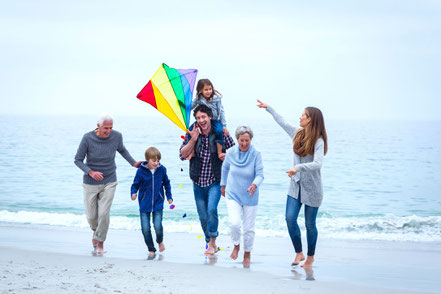 Familie mit Großeltern, Eltern und Kindern lässt am Strand einen Drachen steigen. Alle sind gesund und vital dank einer Darm-Kur.