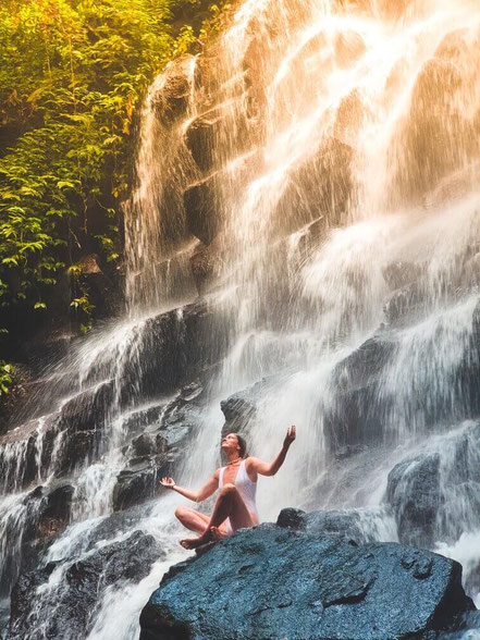 woman in a swimsuit meditating by a large waterfall