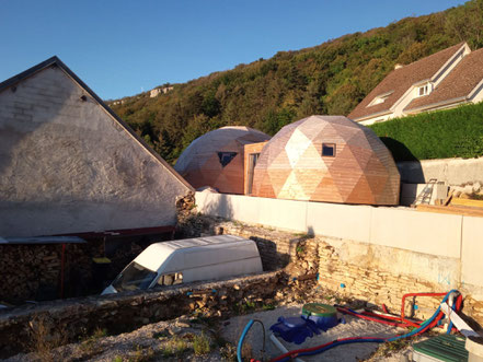 Double dôme géodésique avec connection par un tunnel. Bardage bois et isolation pour ce dôme maison. Ce dôme comporte des ouvertures en double vitrage. Un petit dôme est relié au grand dôme. Isolation en laine de bois.