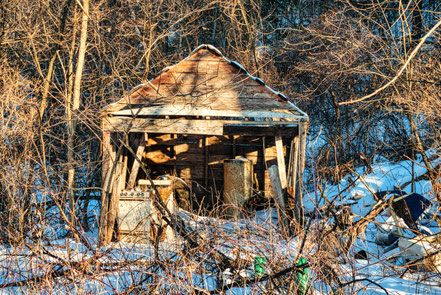 Dilapidated shed in a wooded area with snow covering the ground.