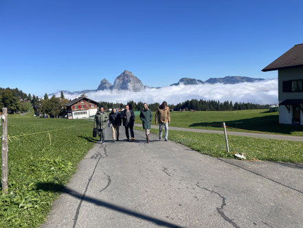 Eine gemischte Gruppe spaziert beim Teamevent mit einem Rätselkoffer durch das Dorf Stoos. Das Outdoor Escape Spiel ist eine Idee für den Teamevent in der Stoos Lodge und kann bei schlechtem Wetter stationär (ohne GPS) gespielt werden.