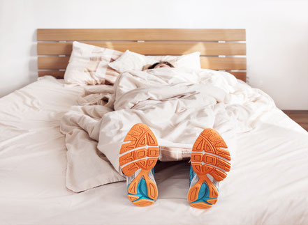 Sportlerin erschöpft liegt mit Turnschuhen im Bett.