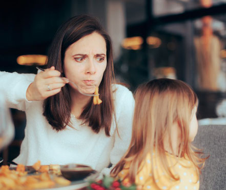 Eine Mutter, die mit ihrer kleinen Tochter im Restaurant beim Essen sitzt und sehr genervt und verbissen schaut, weil sich das Kind abwendet und nichts essen möchte - mein schützling