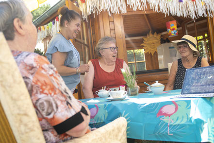 Beohnerinnen sitzen im Sommer vor dem Gartenhaus, haben Spaß und trinken Kaffee