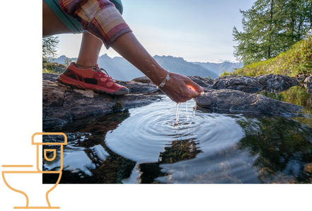 Wasserquelle in der Natur, eine Person beim Wandern hält die Hand ins fließende Wasser.