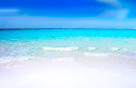 Foto. Oben blauer Himmel. Mitte türkisfarbenes Meer, glatt, nur mit leichten Wellen zum Strand hin.