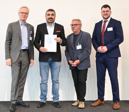 Absolvent zeigt stolz die erhaltene Urkunde beim Gruppenfoto