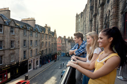 Grassmarket, a historic street in Edinburgh. Three young people on the terrace overlooking the street and terraced houses 