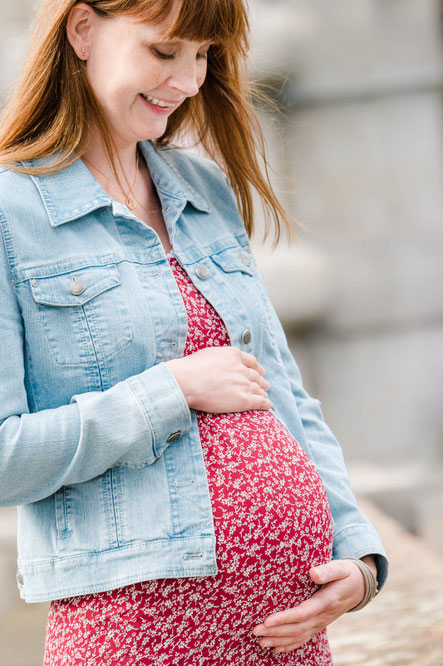 Eine Schwangere hält lachend mit beiden Händen ihren Babybauch fest.